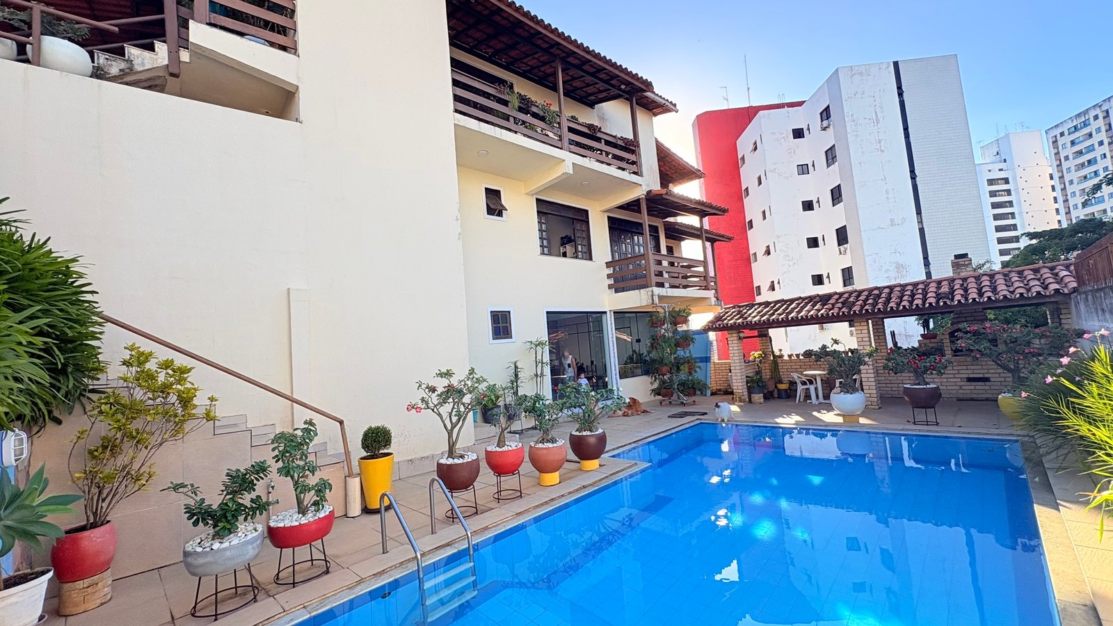 Vista panorâmica da casa da família Pimenta, com piscina, jardim e a porta de vidro do Espaço Terapêutico Chama Violeta